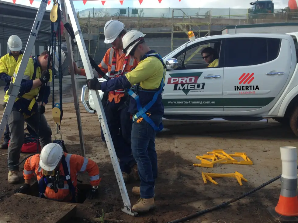 Trainees using a tripod and harness to rescue a worker from a confined space on a construction site
